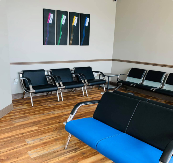 Modern dental waiting room with blue bench seating, black chairs, wooden flooring, and abstract wall art.
