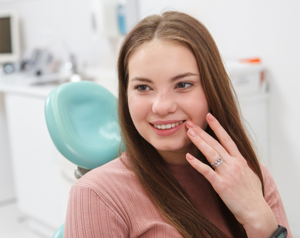 Woman smiling at dental office with turquoise chair visible in background.