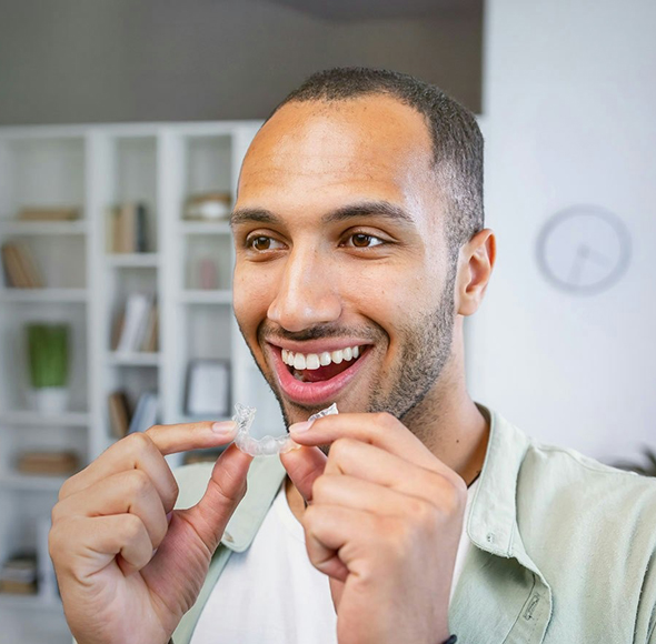 Man smiling brightly while pointing at his teeth in a modern office setting.