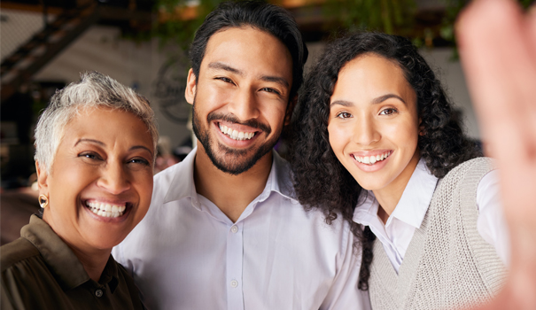 Three smiling people posing together indoors in a warm, friendly group portrait setting.