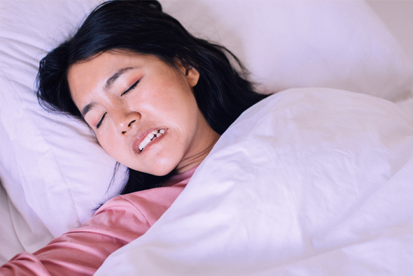 Woman sleeping peacefully in bed with white pillows and bedding, smiling contentedly.