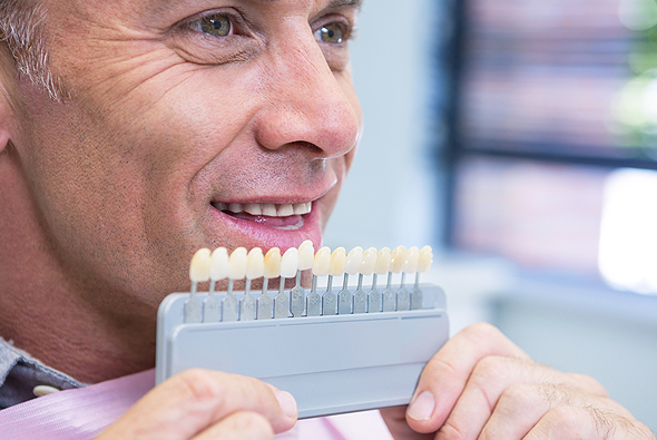 Man examining dental shade guide in clinical setting, smiling at camera.