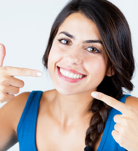 Woman in blue top pointing at her smile against white background