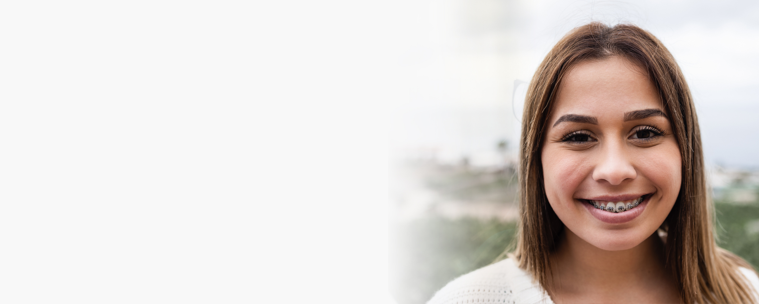 Young woman smiling at camera with blurred outdoor background.
