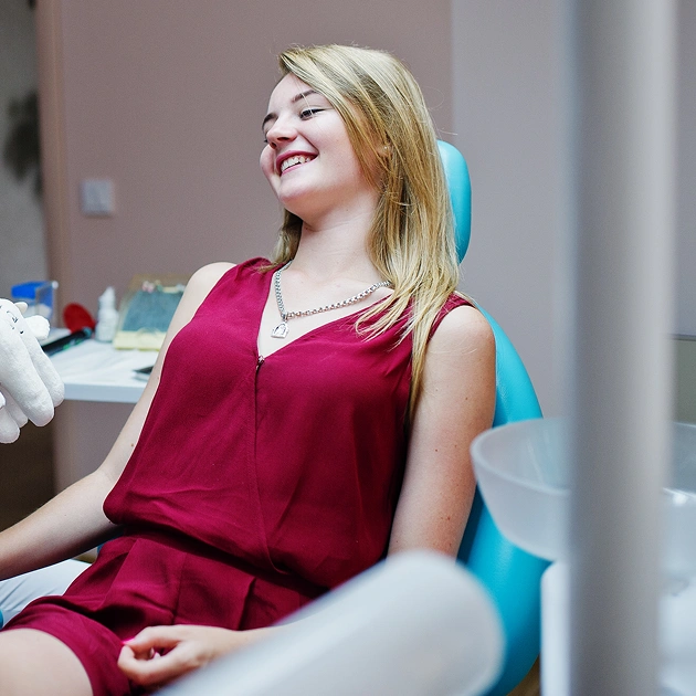 Woman in burgundy top smiling while seated in modern dental office setting.