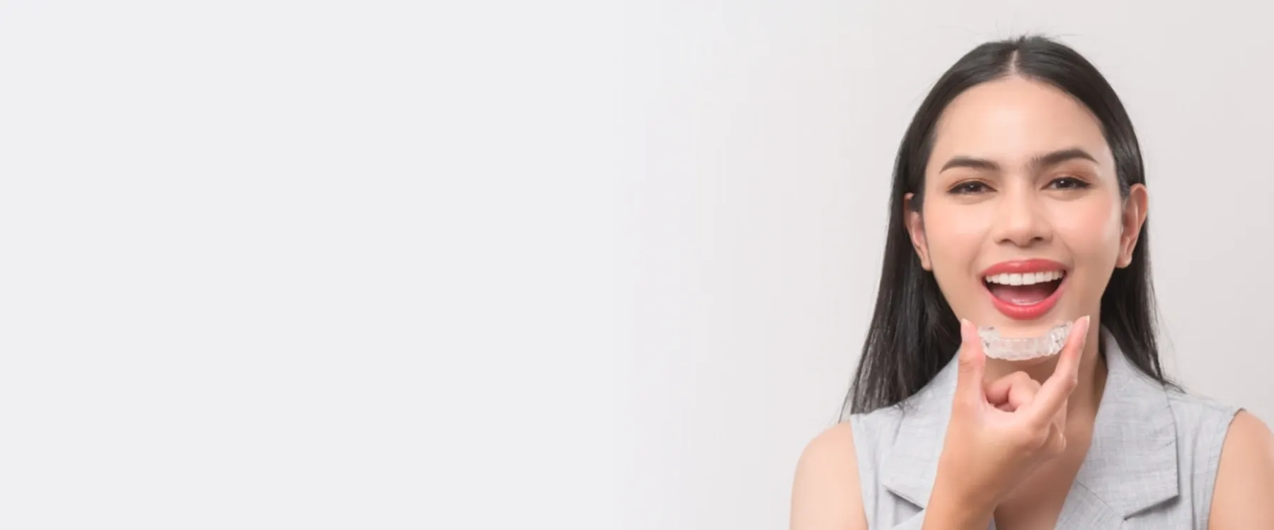 Woman with red lipstick smiling and pointing at chin against white background